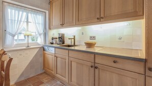 A kitchen with wooden cabinets, a sink, a coffee maker, and a window with curtains. - Green Teft - thatched house in the southwest part of the village of Keitum (Sylt / OT Keitum)
