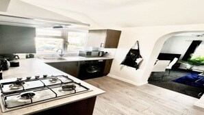 A modern kitchen with a gas stove, microwave, and sink. There is a dining area with a blue rug and a plant.