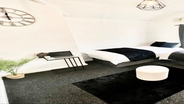A modern hotel room with a large bed, a smaller bed, a desk, a chair, a potted plant, and a window with curtains.