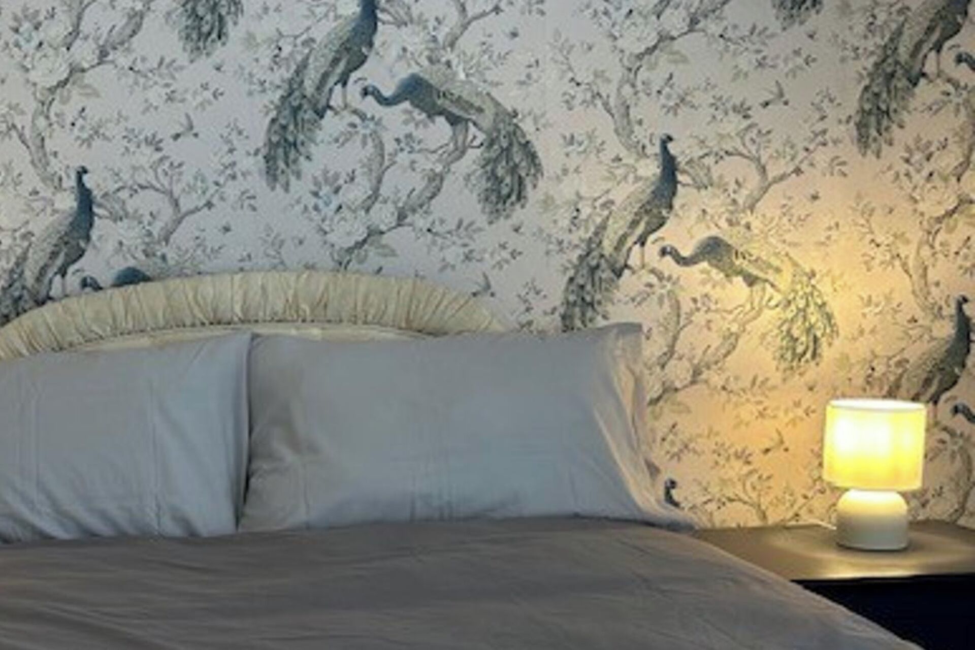 A bed with a white pillow and a nightstand with a lamp.
