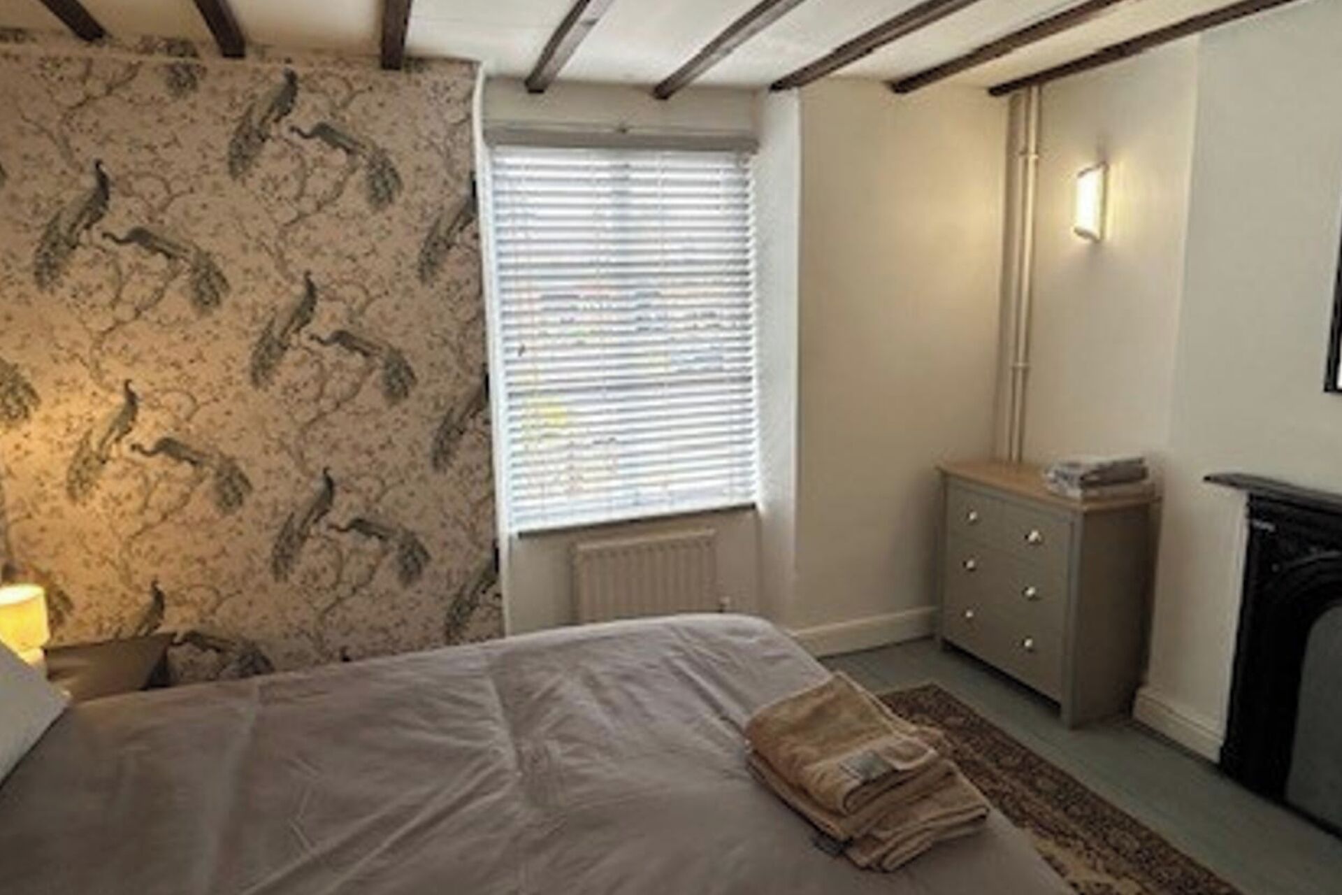Ein Schlafzimmer mit Bett, Heizkörper, Kommode und einem Fenster mit Jalousien.