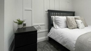 Um quarto com uma cama, mesa de cabeceira e um vaso de planta.