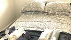 A bed with patterned bedding and pillows, a bedside table with a lamp, and a window with blinds.