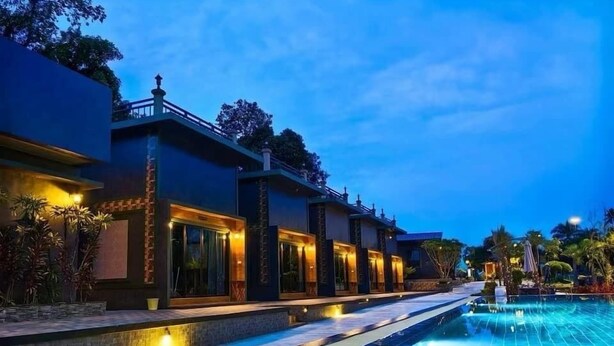 Una piscina con borde de baldosas, rodeada de edificios con iluminación cálida y un cielo despejado.