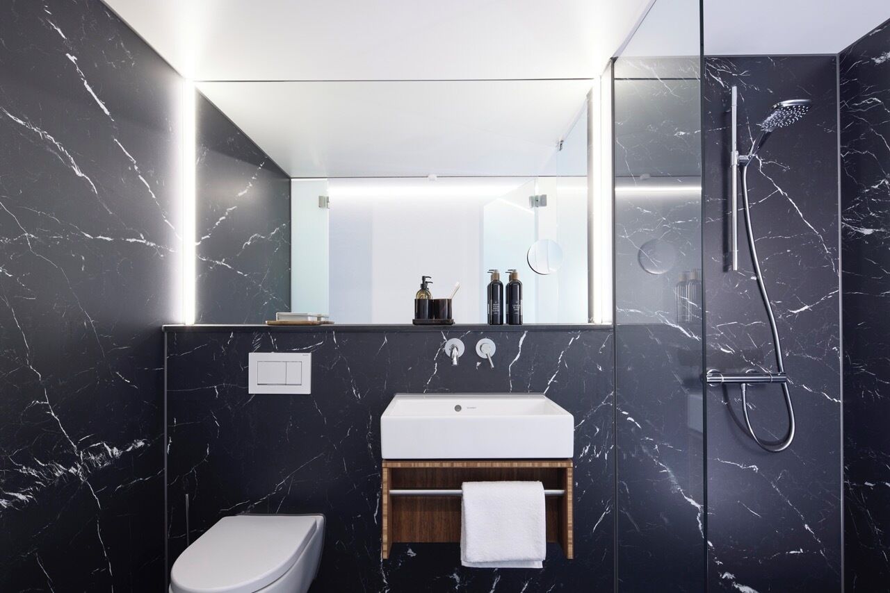 Une salle de bain moderne avec un mur en marbre, un lavabo blanc, des toilettes et une douche séparée par une paroi de verre.