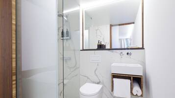 Un baño moderno con cabina de ducha de vidrio, inodoro blanco, lavabo de mármol y un espejo grande.
