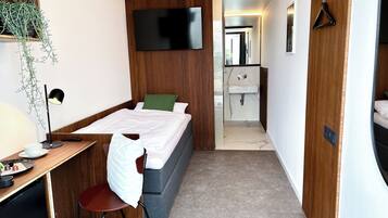 Una habitación de hotel moderna con cama, escritorio, silla, televisión y baño con lavamanos y espejo.