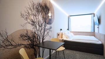 A modern hotel room with a bed, a desk, a chair, and a large window.