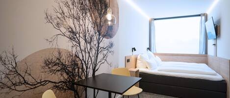 Una habitación de hotel moderna con una cama, un escritorio, una silla y un ventanal grande.
