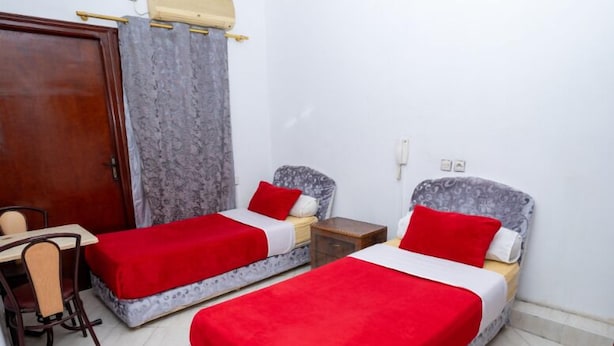 A room with two single beds, each with a red blanket, a wooden desk with a chair, and a grey patterned headboard. - Hotel Alecanti (Beni Mellal)