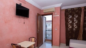 A room with a dining table and chairs, a television mounted on the wall, and a bed with a pink headboard. - Hotel Alecanti (Beni Mellal)