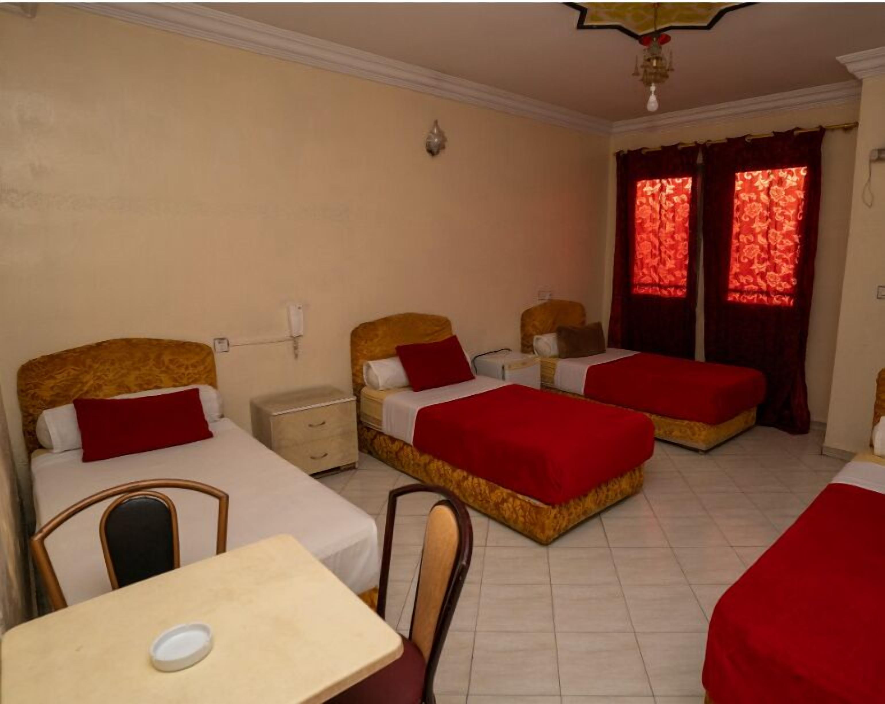 A hotel room with two single beds, a small table, and a chair.