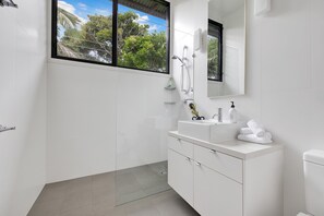 A modern bathroom with a large window, a shower, a sink with a mirror, and a toilet.