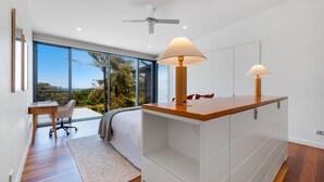 Ein modernes Schlafzimmer mit großem Fenster, Deckenventilator und Nachttisch aus Holz mit Lampe.