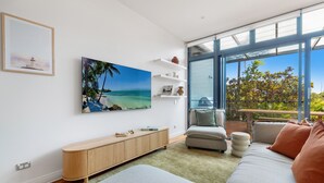Ein modernes Wohnzimmer mit großem Fenster, einem Strandbild, einem Holzkonsolentisch und einer Couch mit Kissen.