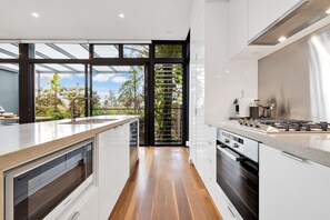 Una cocina moderna con una isla grande, electrodomésticos de acero inoxidable y vistas a zonas verdes a través de amplios ventanales.