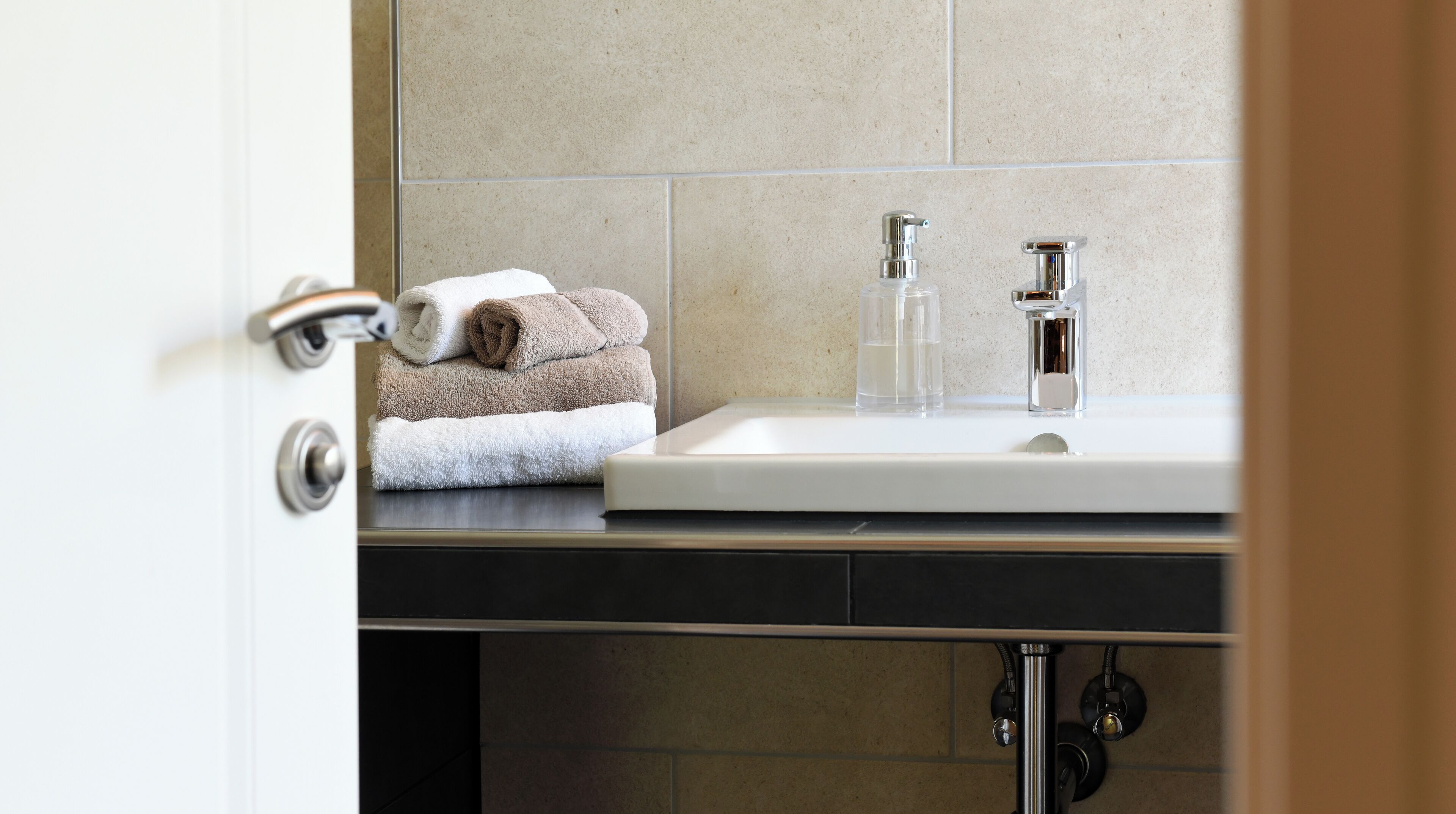 A bathroom with a sink, two faucets, and a towel rack with folded towels.