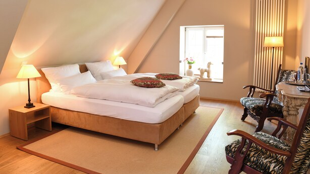Een slaapkamer met een groot bed, twee nachtkastjes met lampen, een raam met gordijnen, en een stoel met een tafel.