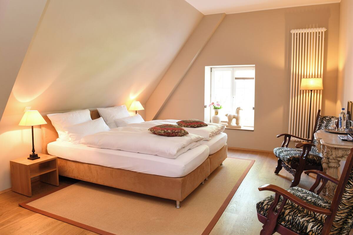 Une chambre avec un grand lit, deux tables de chevet avec des lampes, une fenêtre avec des rideaux et une chaise avec une table.