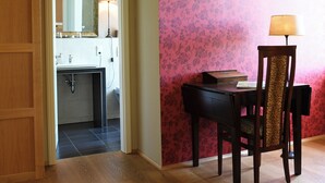 Een kamer met een houten bureau, een stoel met een kussen met luipaardprint, een lamp en een spiegel aan de muur.
