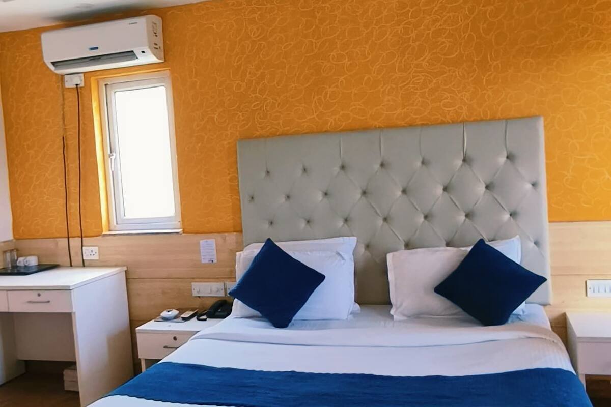 A hotel room with a large bed, a ceiling fan, an air conditioning unit, a desk, and a window.