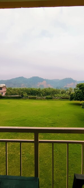 A grassy field with a building in the background and a hill. - Limewood Riverside Resort (Ramnagar)