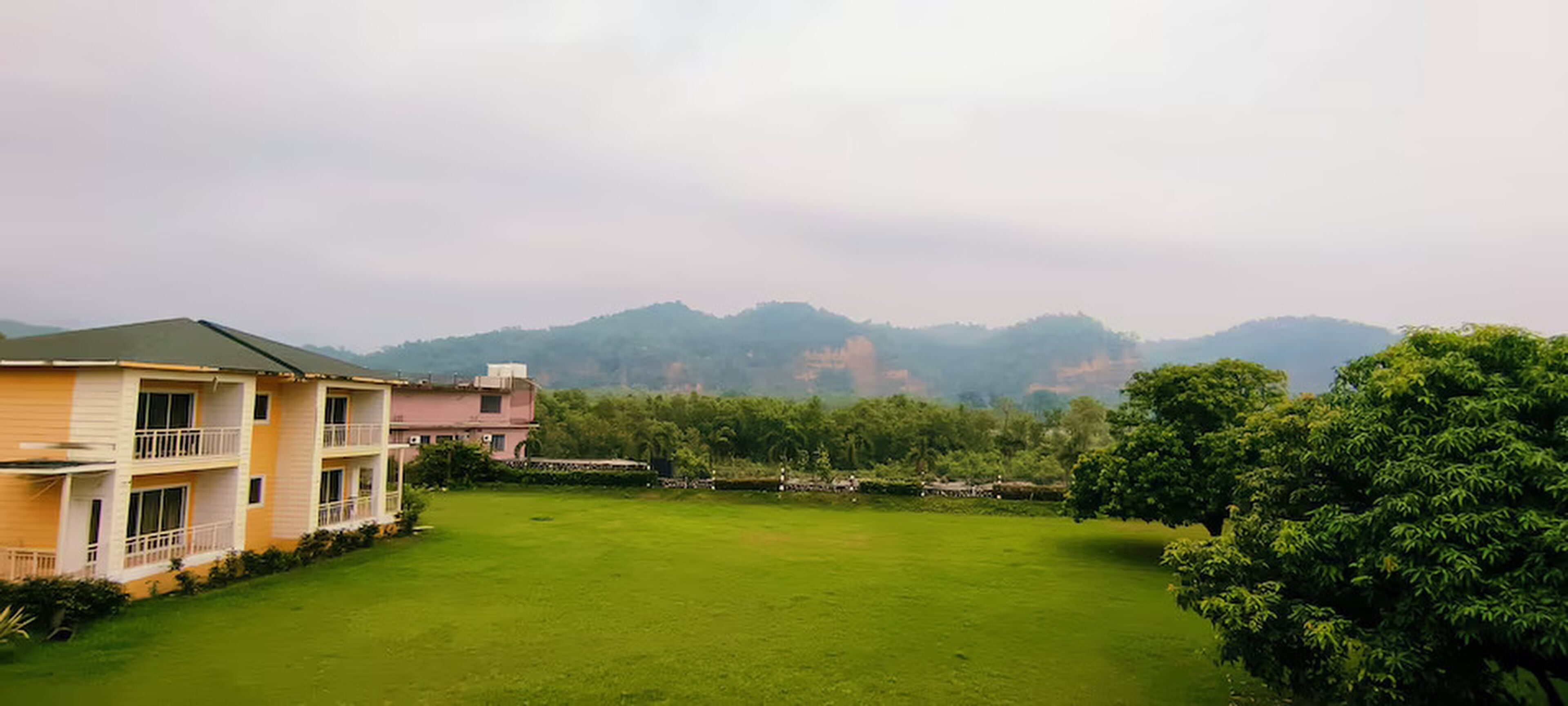 A building with a green lawn in front, surrounded by trees and hills in the background.