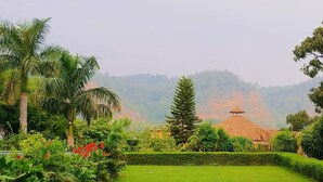 A well-maintained grassy lawn with a variety of tropical plants and a small building with a thatched roof in the background. - Limewood Riverside Resort (Ramnagar)