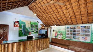 A reception area with a bamboo reception desk, a large poster of a waterfall, and a ceiling with a thatched roof. - Limewood Riverside Resort (Ramnagar)