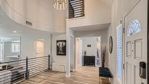 A spacious hallway with a wooden floor, a black bench, and a staircase leading to an upper level. - Spacious Villa 20 min to Strip & Airport!  Private Pool and amenities for all ages! (Las Vegas)