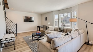 A living room with a sofa, a coffee table, a TV, and a staircase. - Spacious Villa 20 min to Strip & Airport!  Private Pool and amenities for all ages! (Las Vegas)