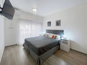 A modern bedroom with a large bed, bedside tables, a flat-screen TV, and a window with sheer curtains. - Modern Studio With Amenities in the Heart of the City (Buenos Aires)