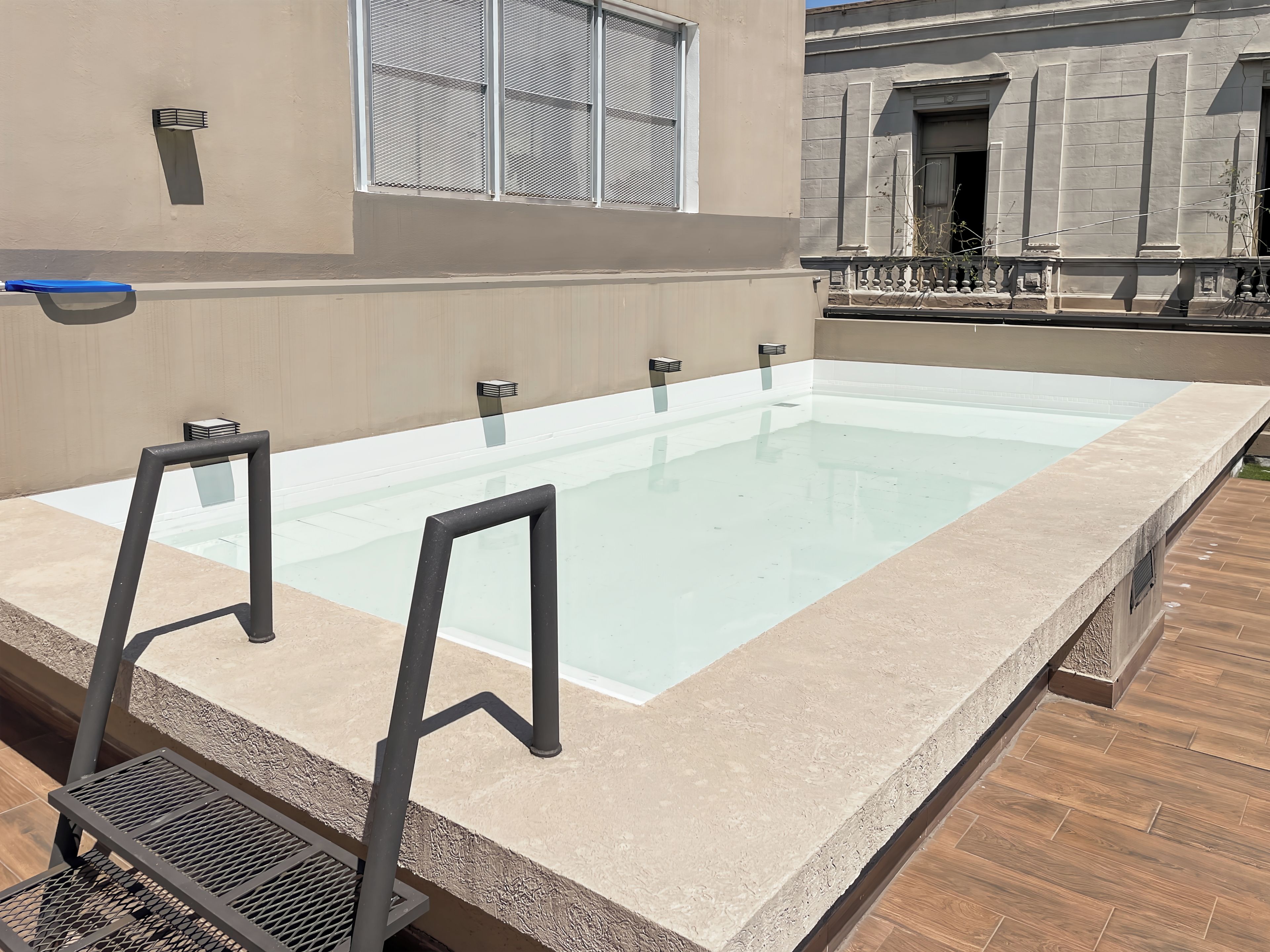 Una piscina rettangolare all'aperto con un bordo piastrellato color beige, circondata da un pontile in legno.
