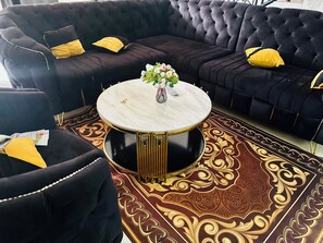 A black leather sofa with gold accents, a round marble coffee table, and a patterned rug.