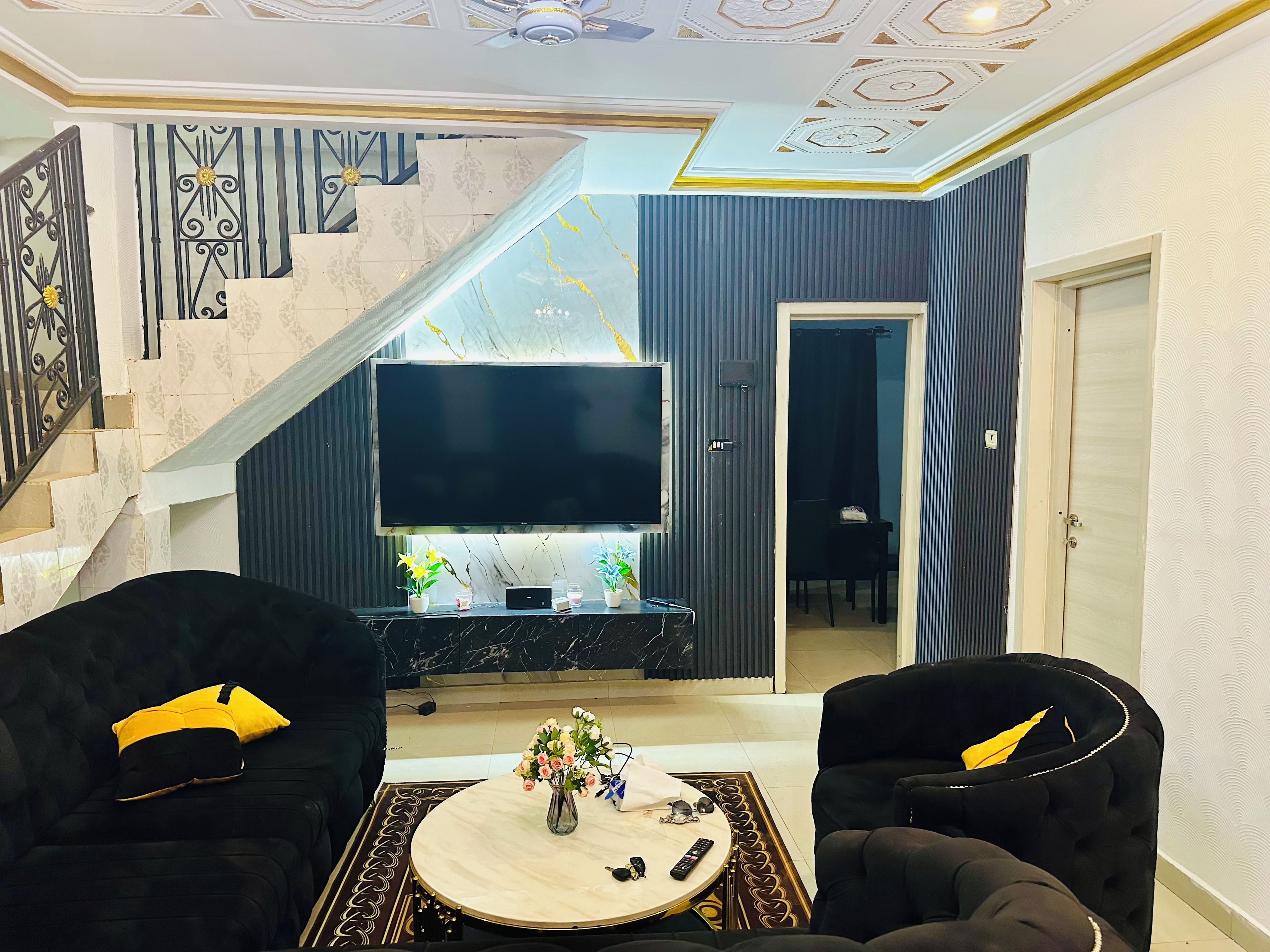 Een woonkamer met een flatscreen televisie, twee zwarte banken, een salontafel en een trap met decoratieve tegels.