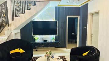 Een woonkamer met een flatscreen televisie, twee zwarte banken, een salontafel en een trap met decoratieve tegels.