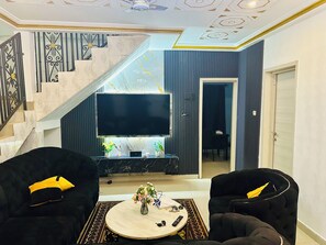 A living room with a flat-screen TV, two black sofas, a coffee table, and a staircase with patterned tiles. - Villa Amina Splendid and Elegant (Ouagadougou)