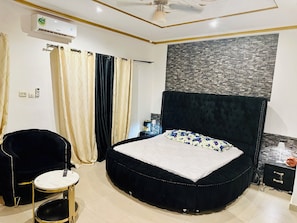 A bedroom with a round bed, a black upholstered chair, a small round table, and a wall-mounted air conditioner. - Villa Amina Splendid and Elegant (Ouagadougou)