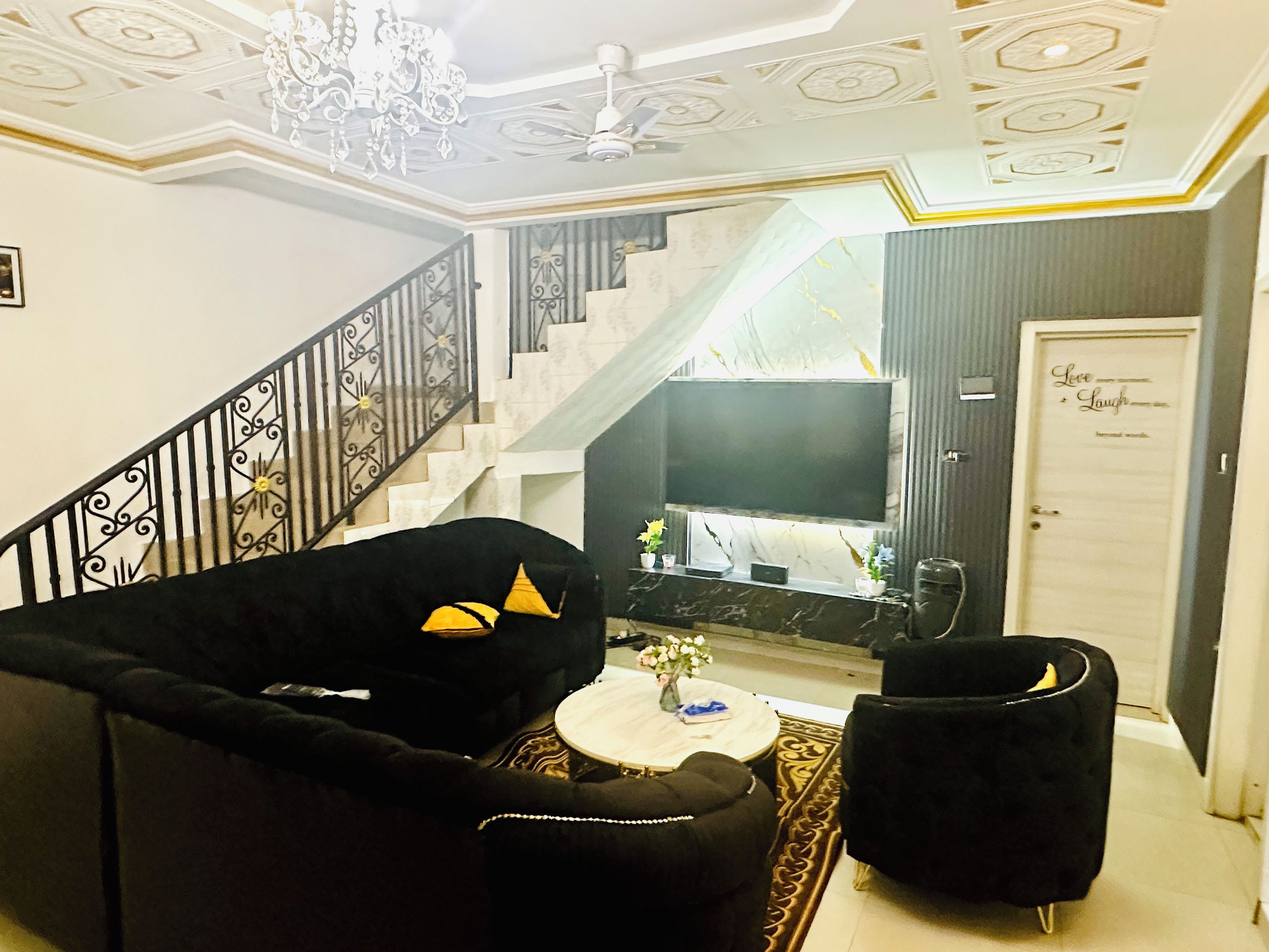 Un salon avec un escalier, un téléviseur et une porte sur laquelle est apposée une pancarte.