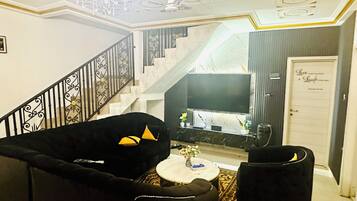 Un salon avec un escalier, un téléviseur et une porte sur laquelle est apposée une pancarte.
