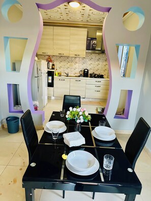 A dining area with a black table set for four, surrounded by chairs, with a kitchen visible through an archway. - Villa Amina Splendid and Elegant (Ouagadougou)
