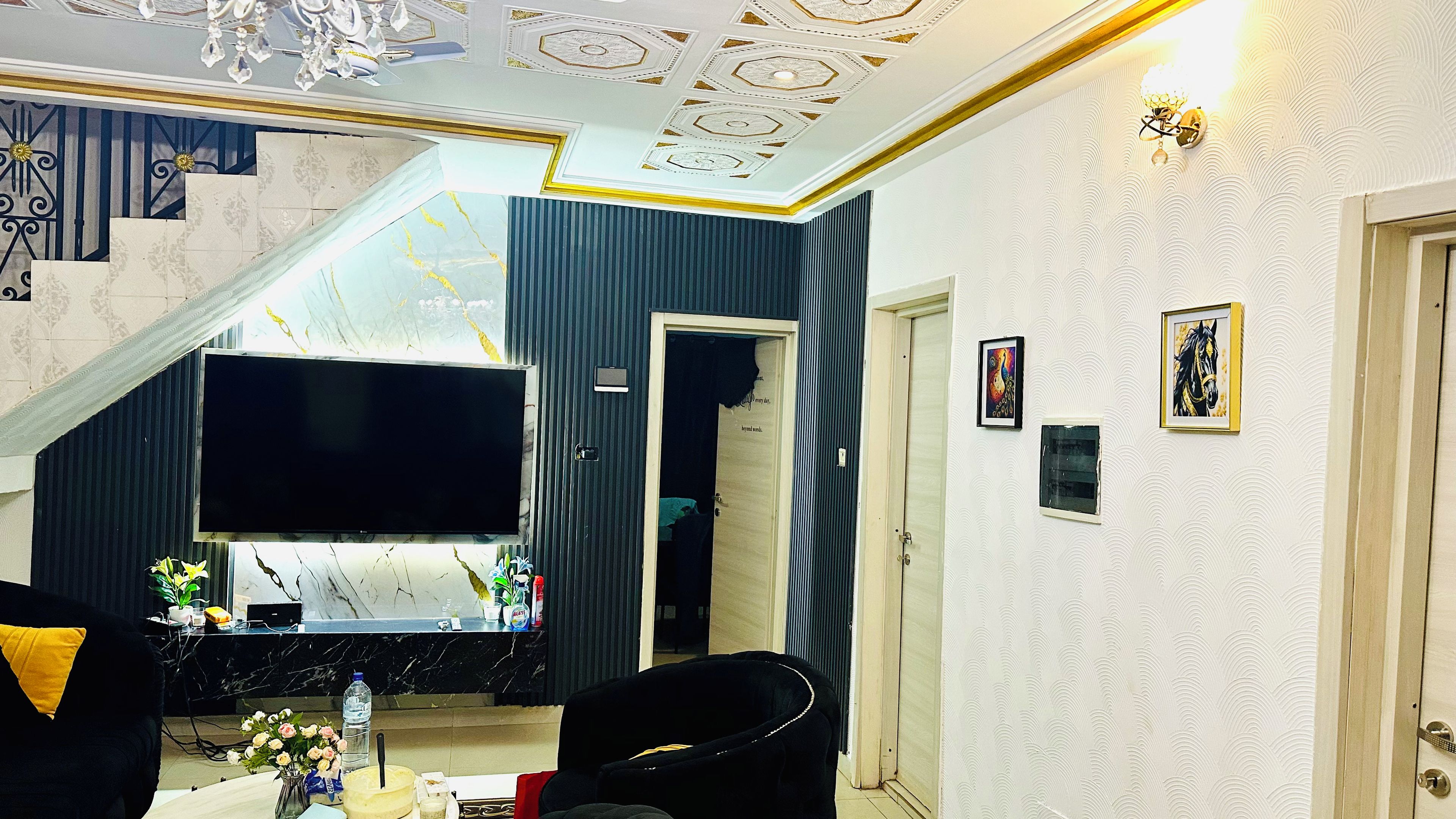 A living room with a large flat-screen TV, a staircase, and a door leading to another room.