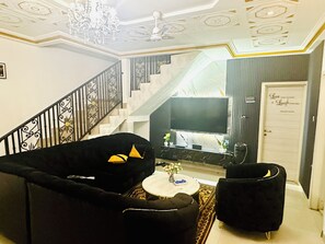 A living room with a staircase, a flat-screen TV, and a door with a sign. - Villa Amina Splendid Elegant Structure (Ouagadougou)
