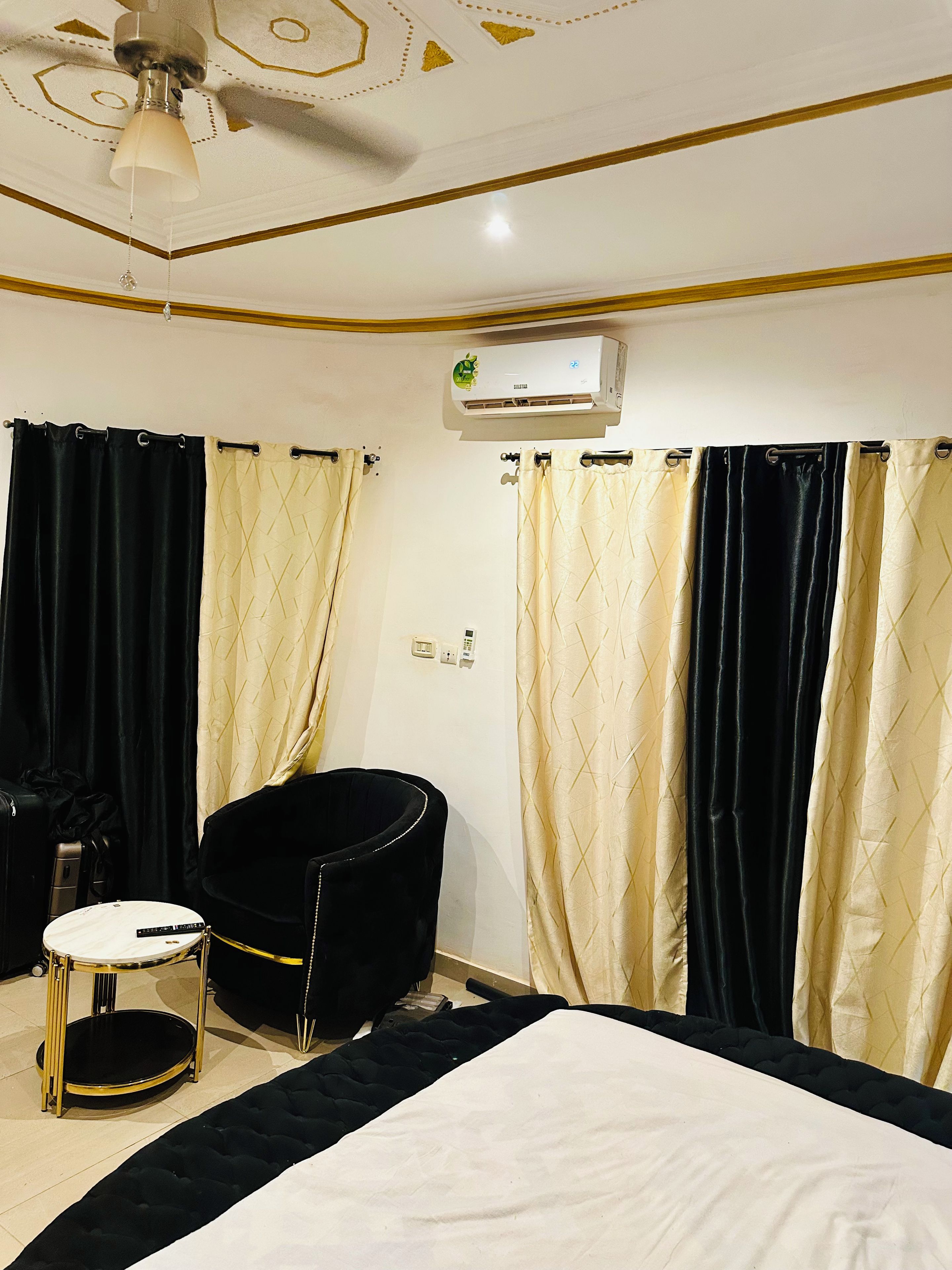 A hotel room with a bed, a chair, a small table, and a ceiling fan.