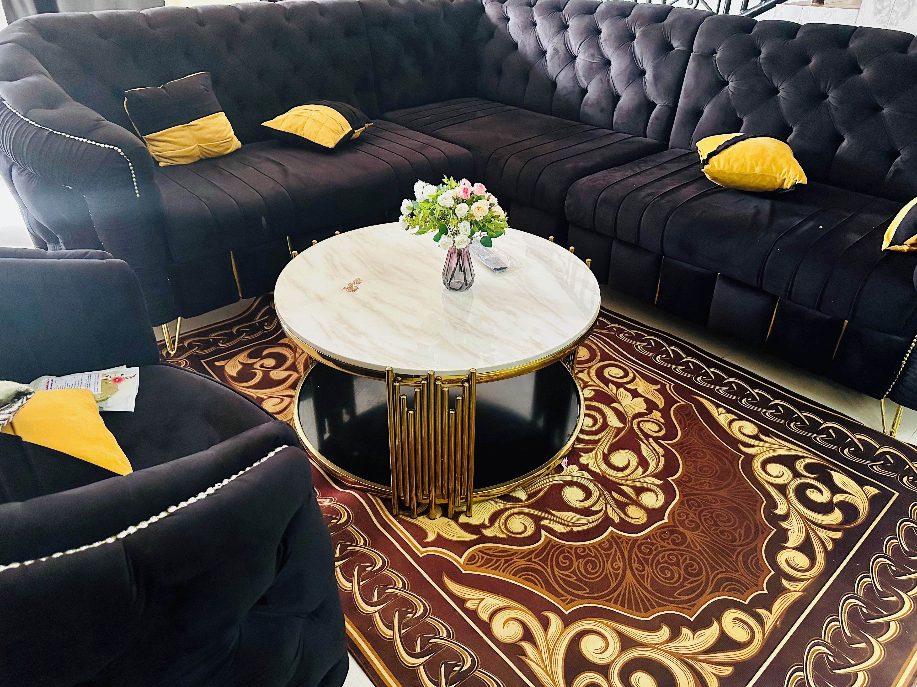 Un canapé noir agrémenté de détails dorés et une table basse ronde dont le plateau est en marbre.