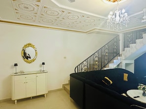 A room with a staircase, a black sofa, a white cabinet, and a mirror with a gold frame. - Villa Amina Splendid Elegant Structure (Ouagadougou)