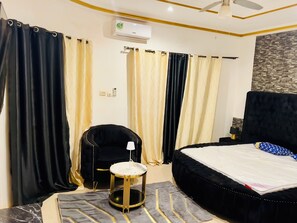 A hotel room with a bed, a chair, a small table, and curtains. - Villa Amina Splendid Elegant Structure (Ouagadougou)
