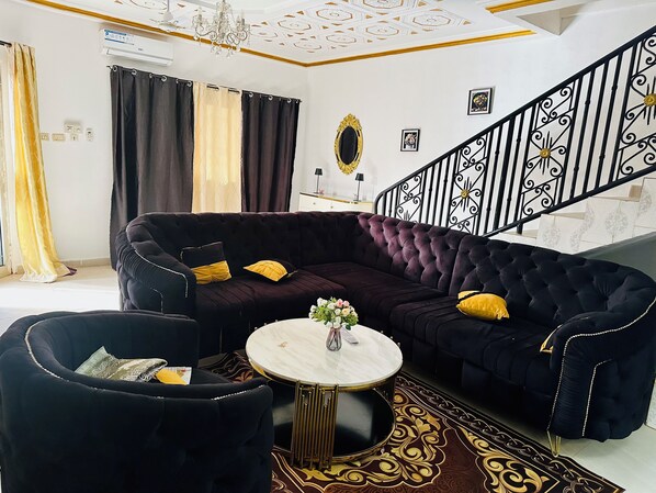 Una sala de estar con un sofá oscuro, una mesa de centro redonda y una alfombra estampada.