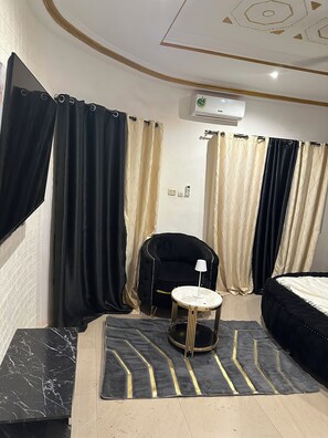 A room with a black and beige curtain, a black armchair, a round table with a lamp, and a bed. - Villa Amina Splendid Elegant Structure (Ouagadougou)