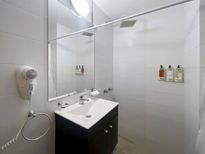 Egy modern fürőszoba, melyben fehér mosdókagyló, tükör és a falra szerelt, kézi használatú hajszárító található.